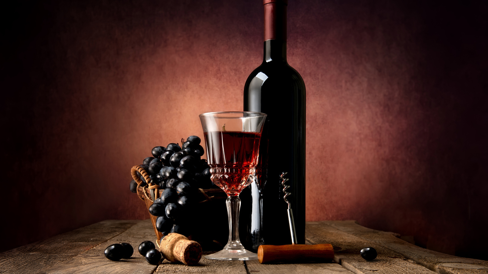 Бутылка красного вина на столе с бокалом и синим виноградом