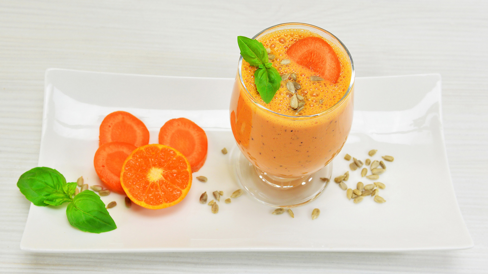 Бокал морковного коктейля с апельсином на белой тарелке