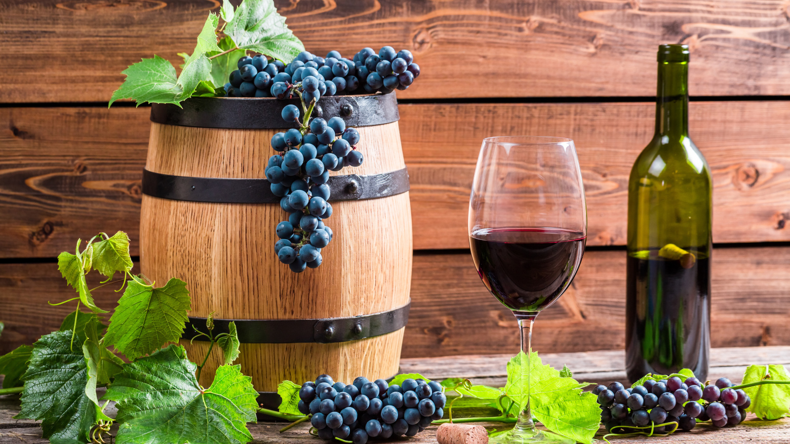 Бокал вина с бочкой и бутылкой на столе с гроздьями синего винограда с листьями