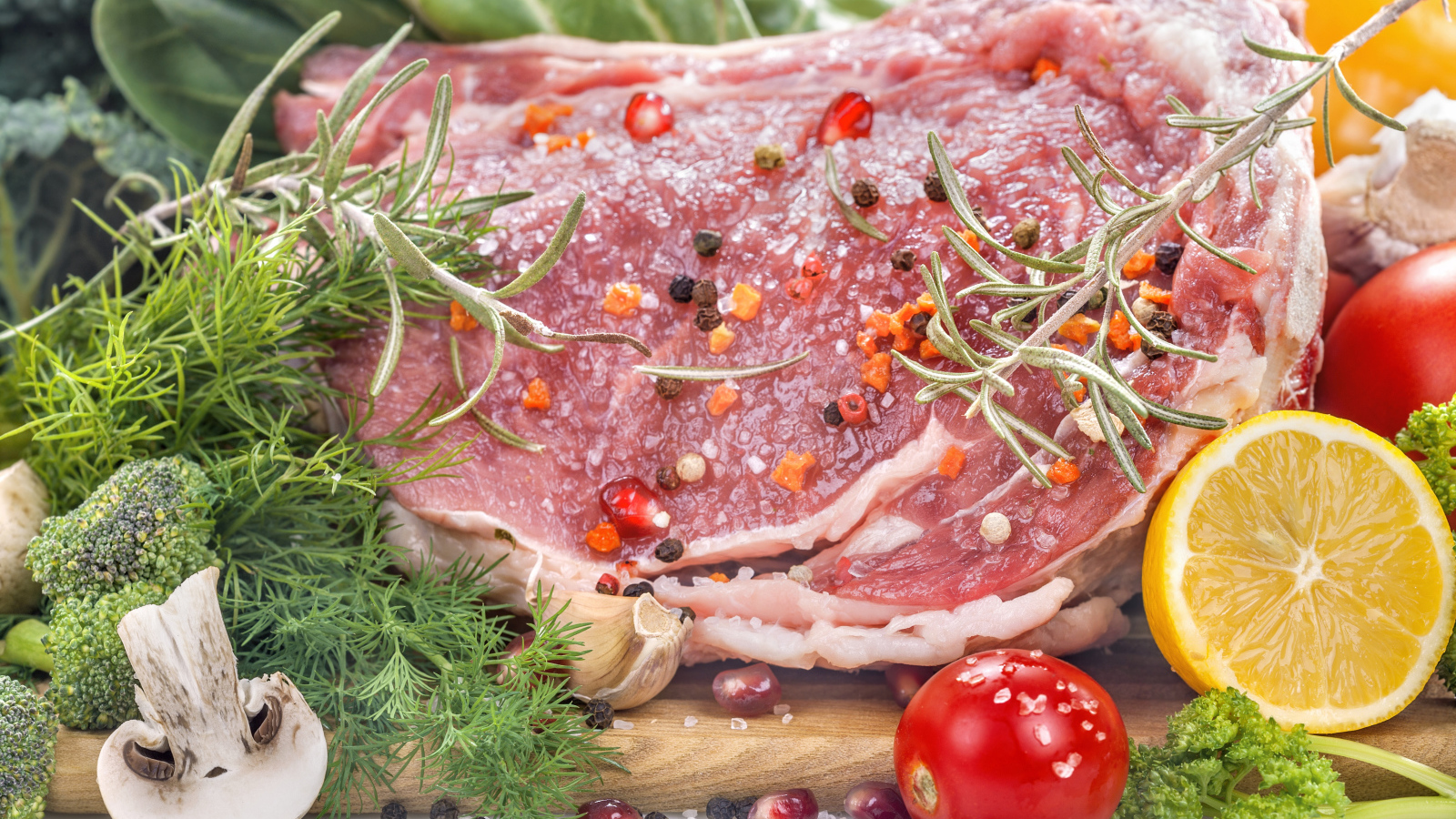 Кусок свежего мяса со специями и зеленью на разделочной доске