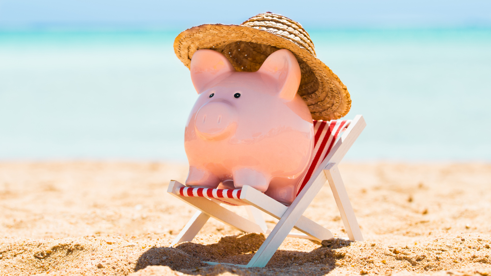 Сувенир свинка в шляпе лежит в игрушечном кресле на пляже