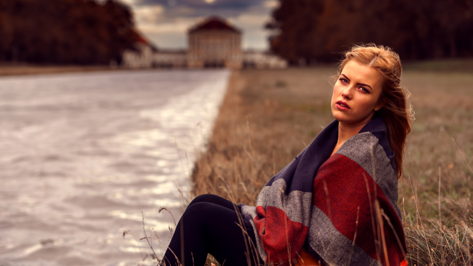 Девушка в пледе сидит на берегу реки