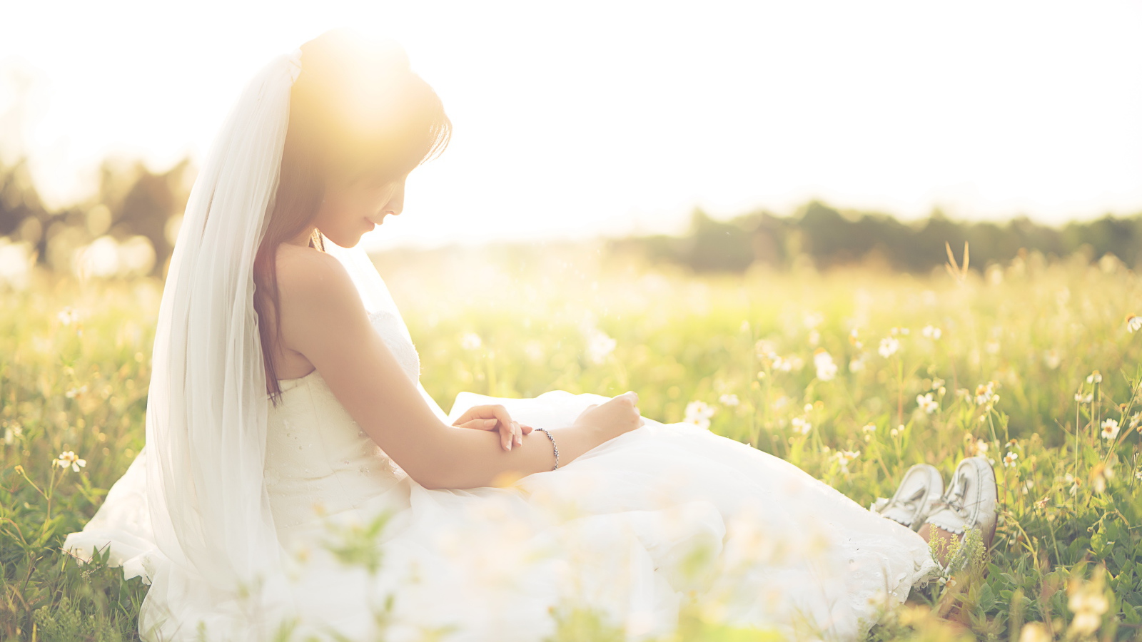 Девушка азиатка в платье невесты сидит на траве в поле 