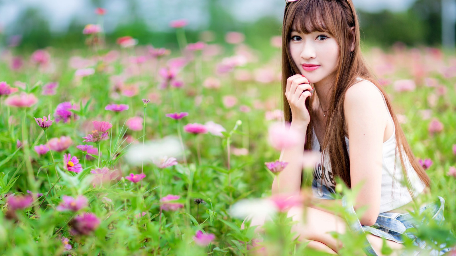 Красивая девушка модель азиатка на поле с розовыми цветами