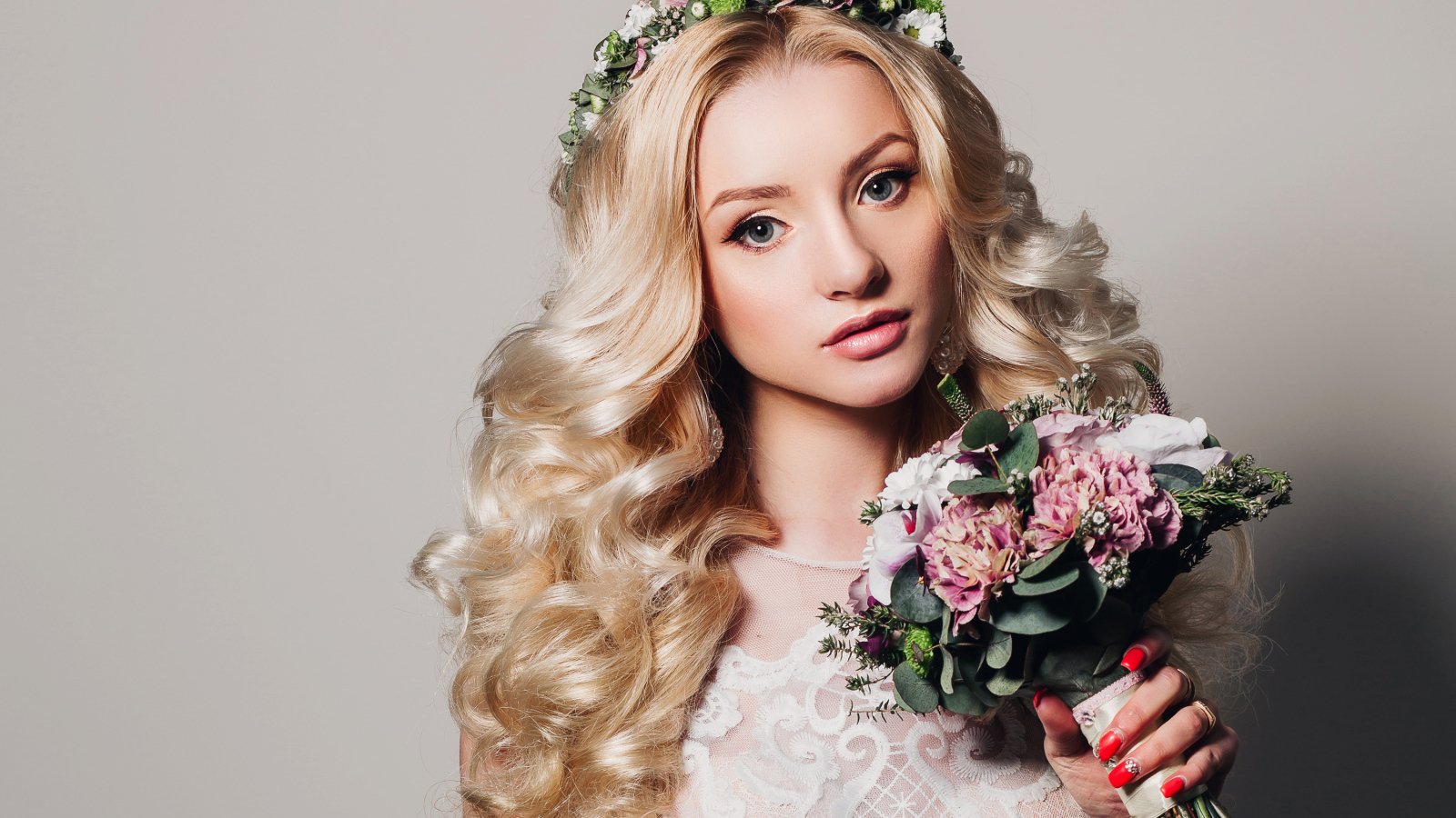 Красивая блондинка в свадебном платье с букетом цветов на сером фоне