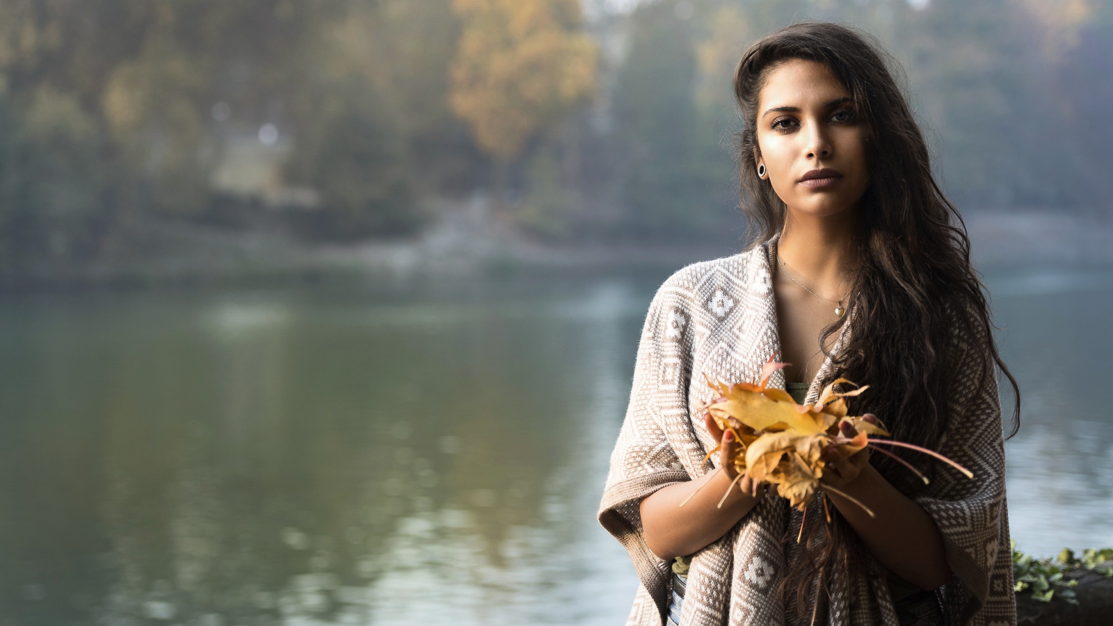 Красивая брюнетка у реки с желтыми листьями в руках
