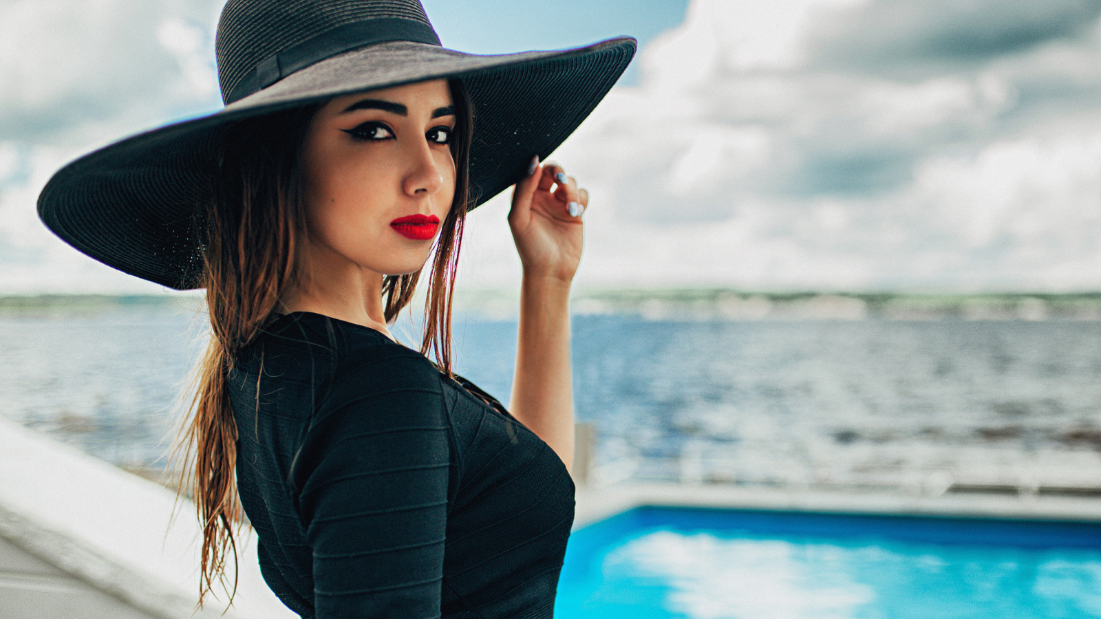 Красивая девушка в большой черной шляпе у бассейна
