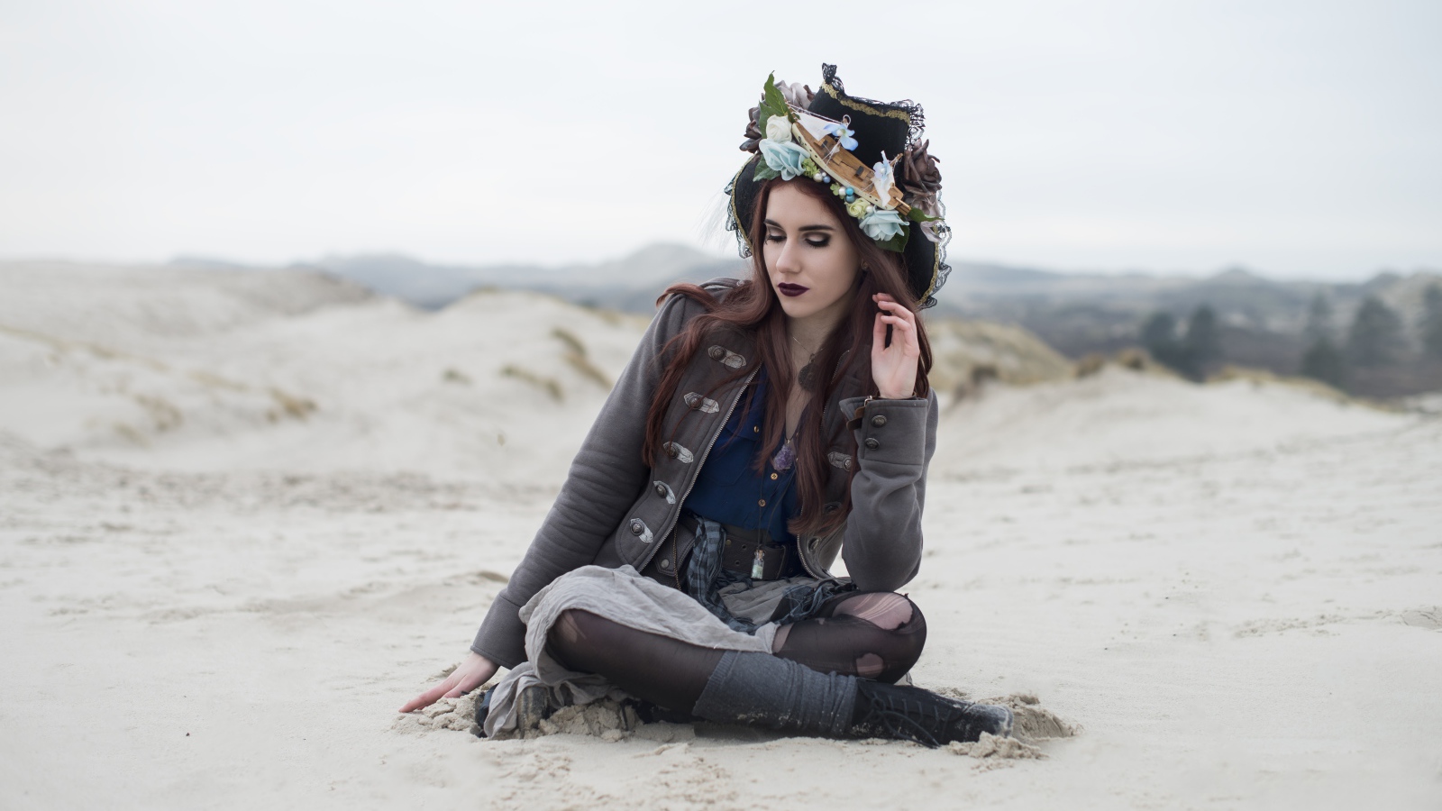 Девушка брюнетка  в костюме сидит на песке 