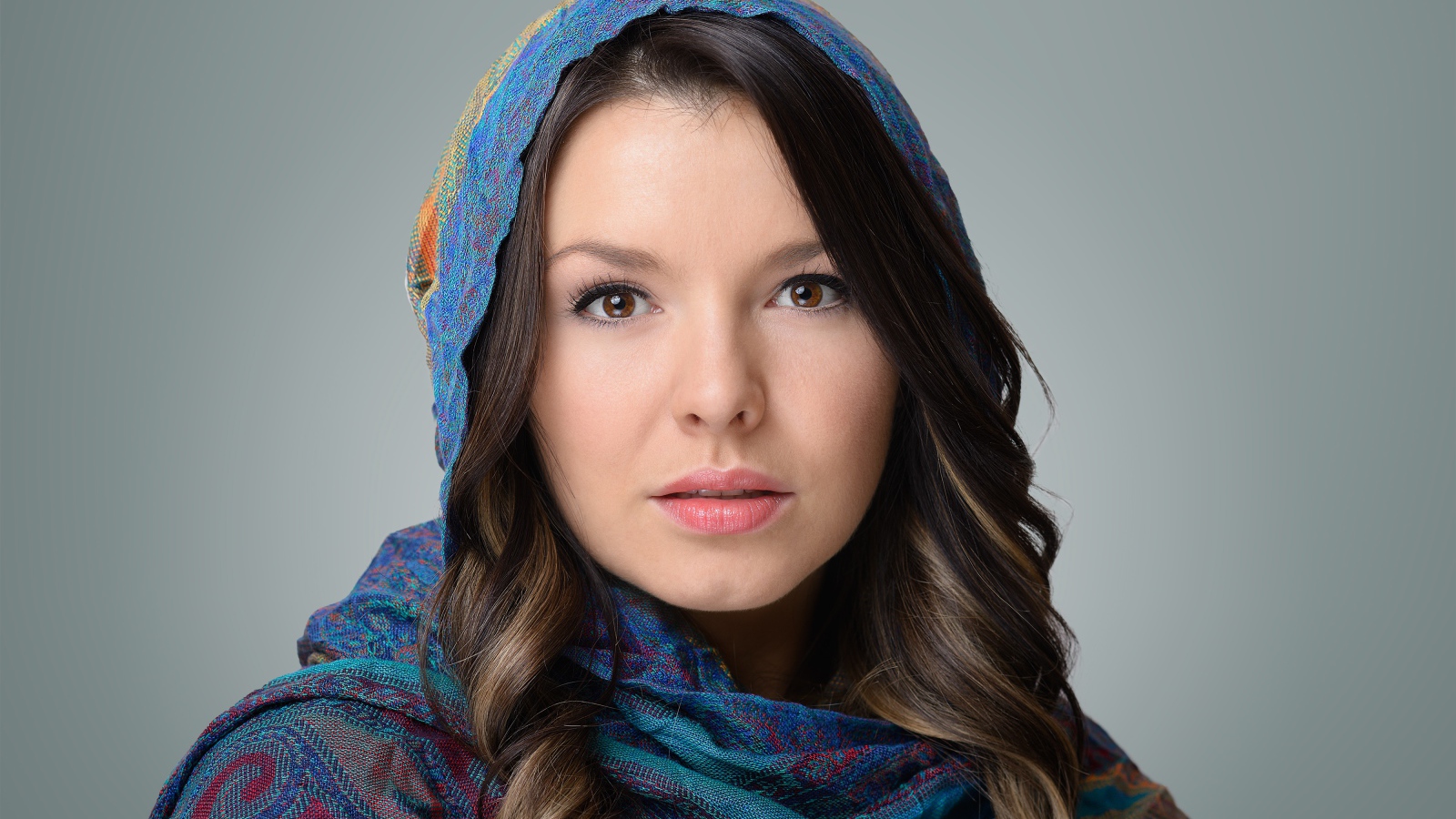 Лицо молодой кареглазой девушки в платке на сером фоне