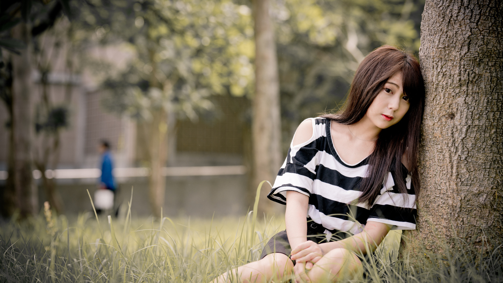 Молодая девушка азиатка сидит на траве у дерева