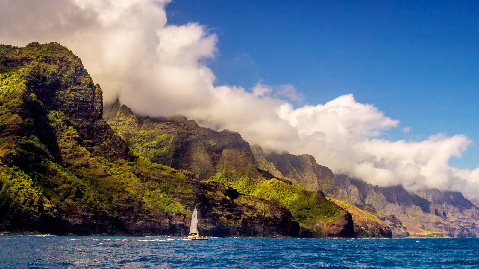 Парусная лодка плывет по голубой воде на фоне покрытых зеленью гор