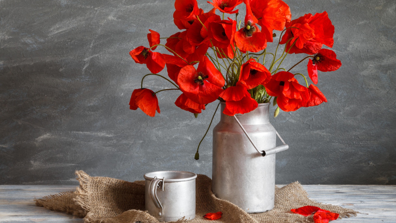 Букет красных маков в железном бидоне на столе с кружкой