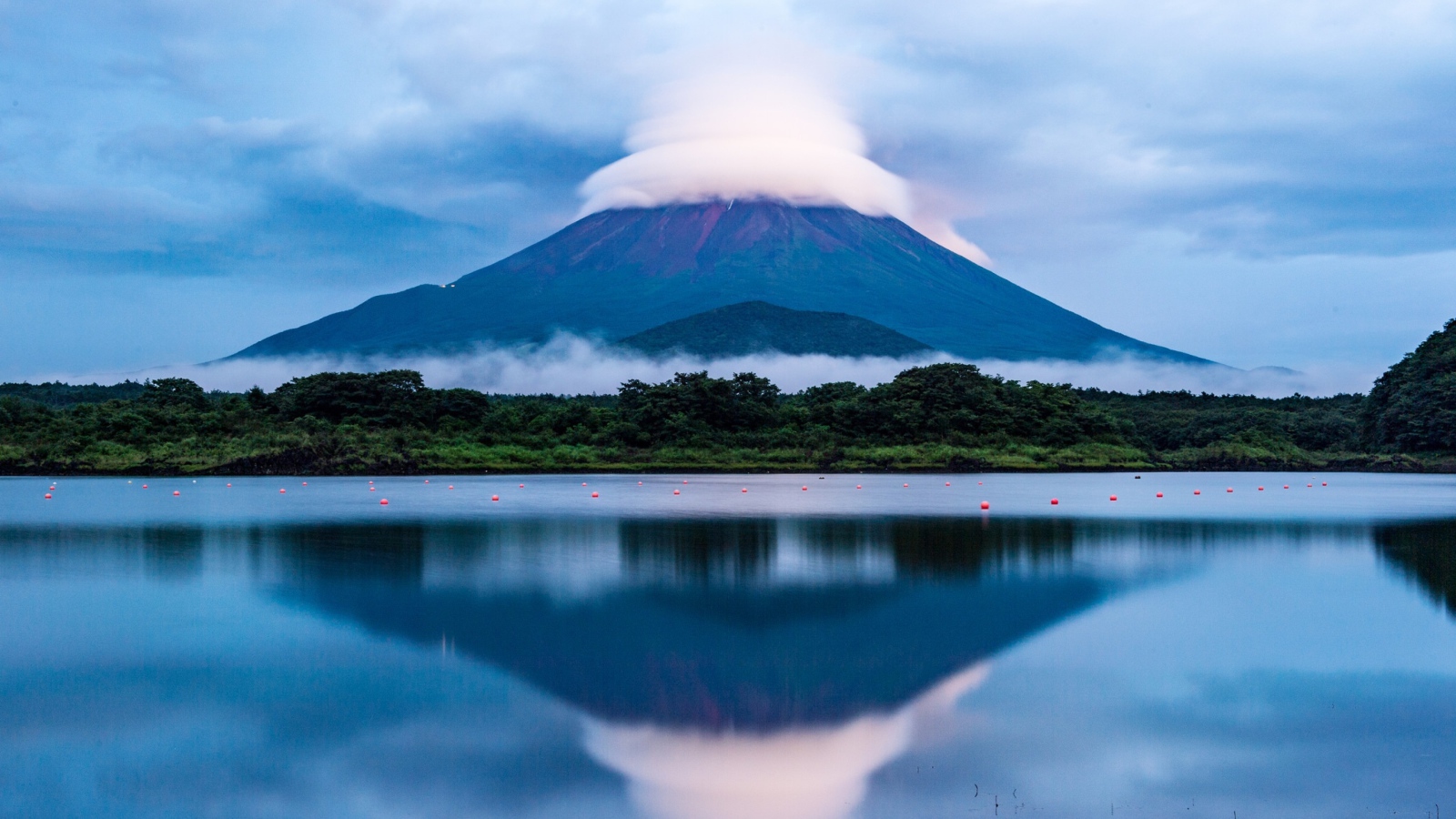 Вулкан Фудзияма в белых облаках отражается в воде озера