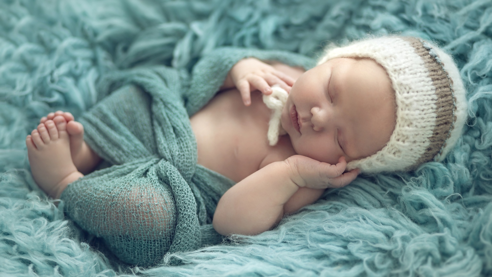 Грудной ребенок спит на зеленом меховом покрывале