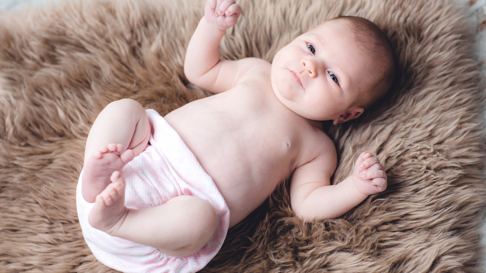Грудной ребенок лежит на меховом покрывале