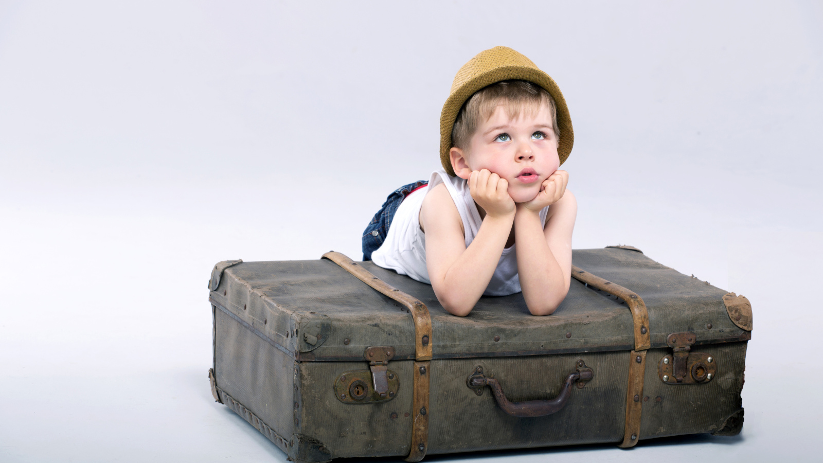 Маленький мальчик лежит на большом чемодане на сером фоне