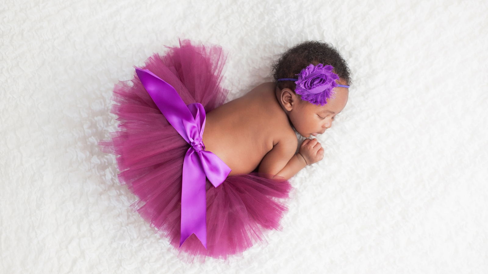 Маленькая девочка в красивой пышной юбке спит на белом покрывале