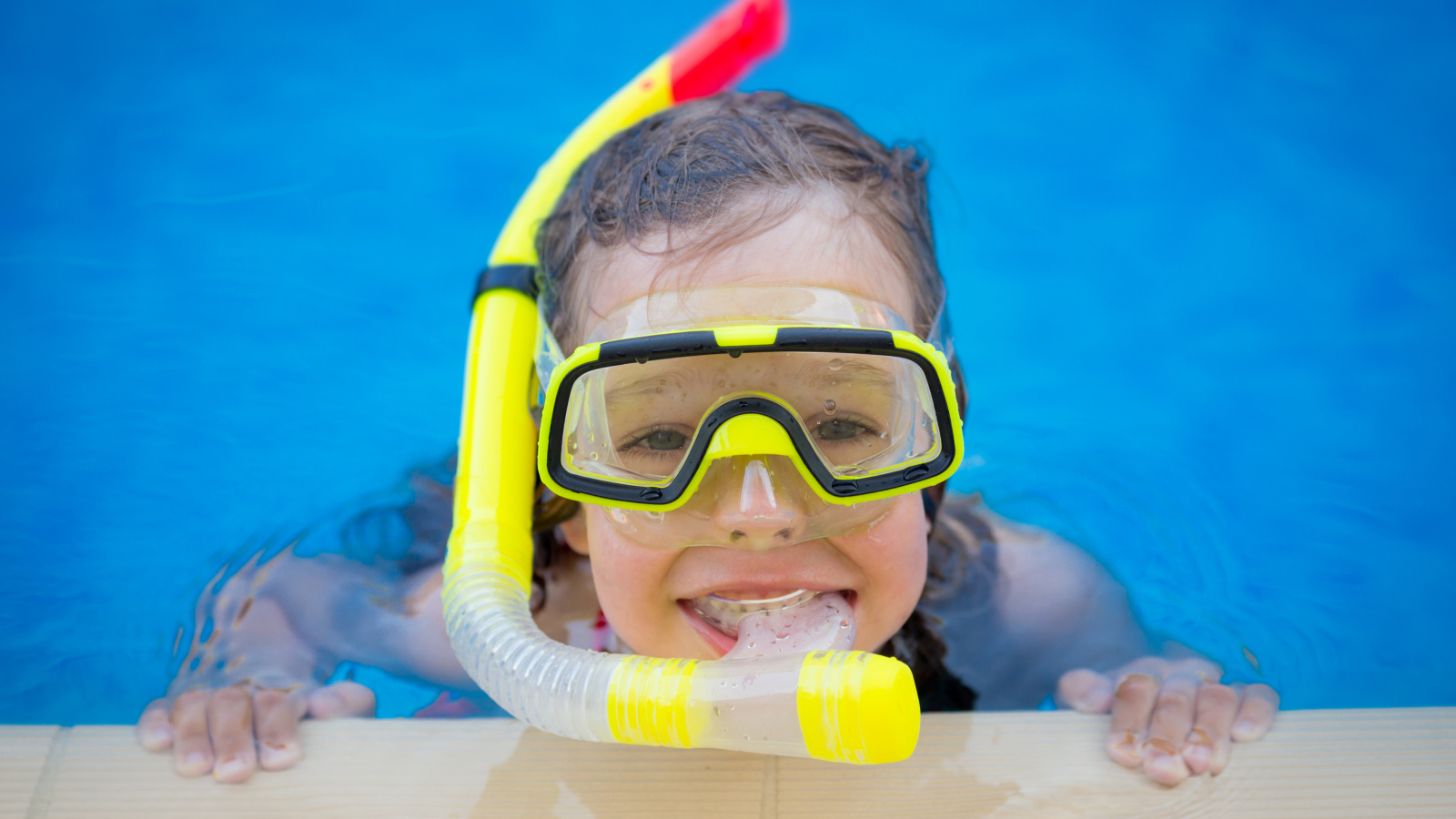 Маленькая девочка в маске с трубкой плавает в бассейне