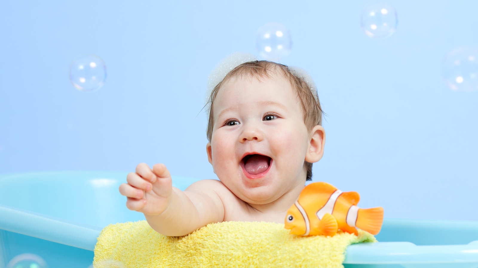 Веселый малыш купается в ванной с игрушечной рыбкой