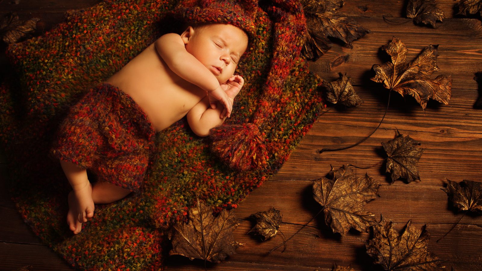 Маленький ребенок спит в вязаном костюме на полу с сухими листьями