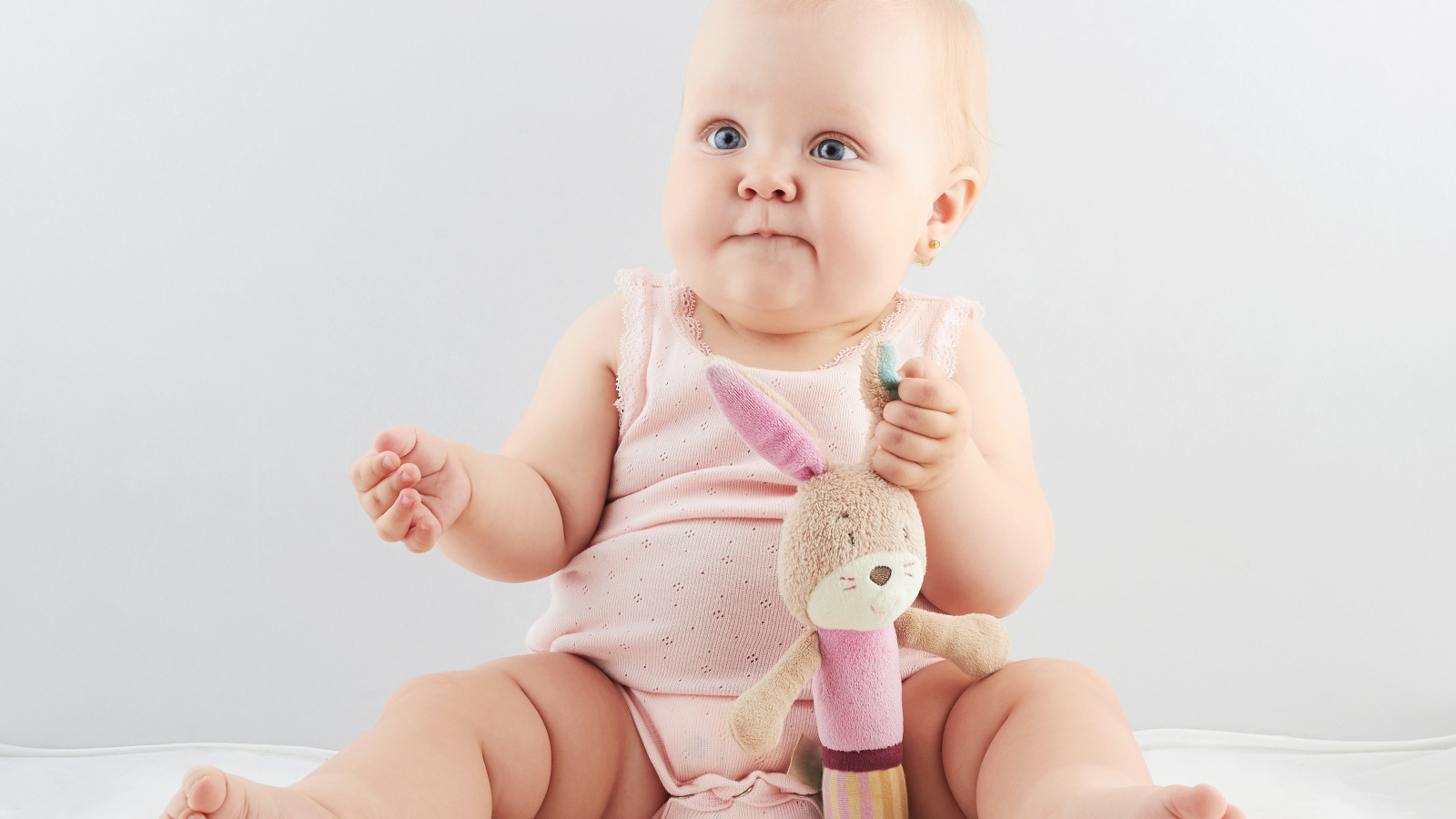 Голубоглазый младенец с мягкой игрушкой на сером фоне
