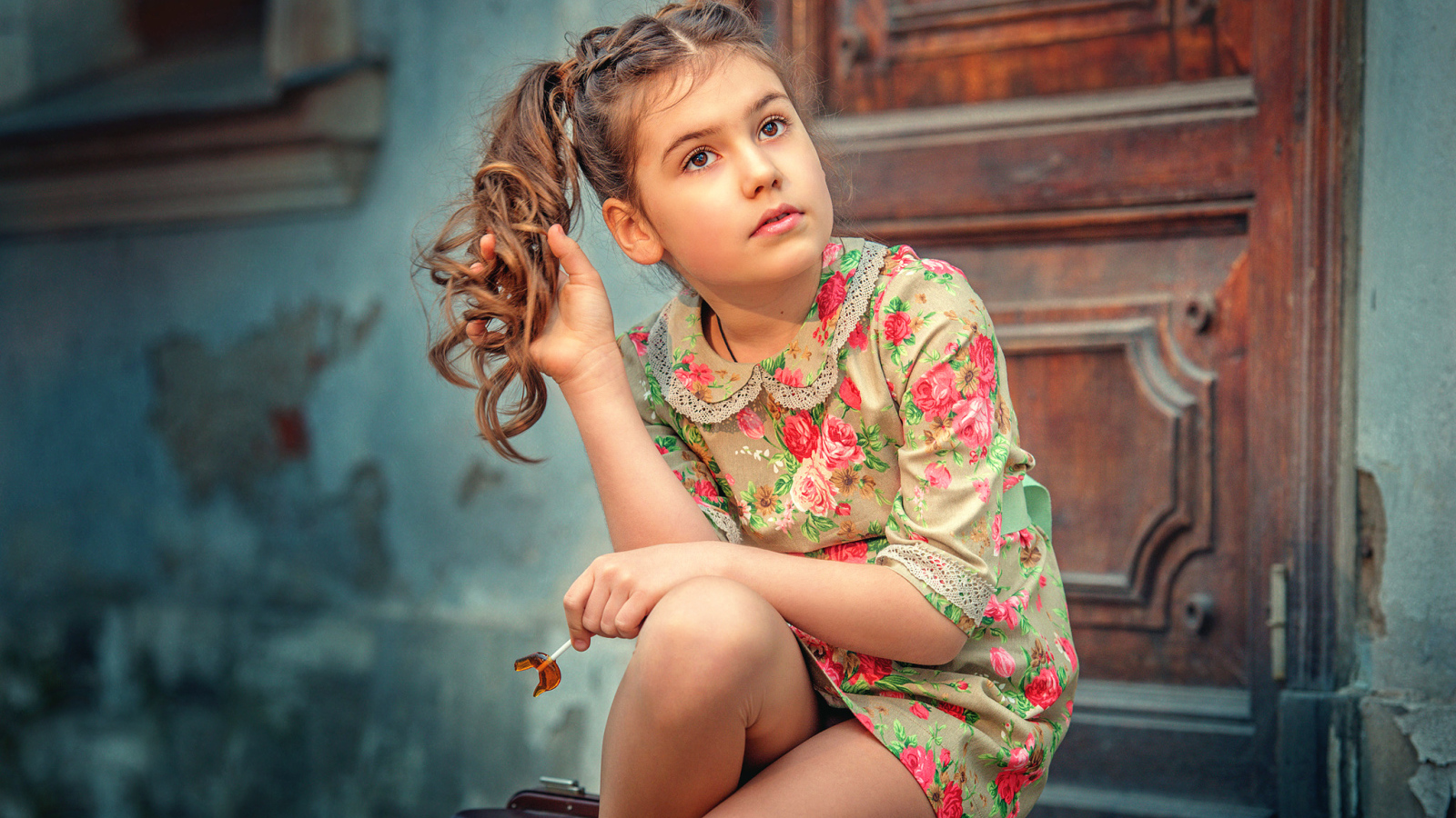 Кареглазая девочка в цветастом платье сидит на пороге
