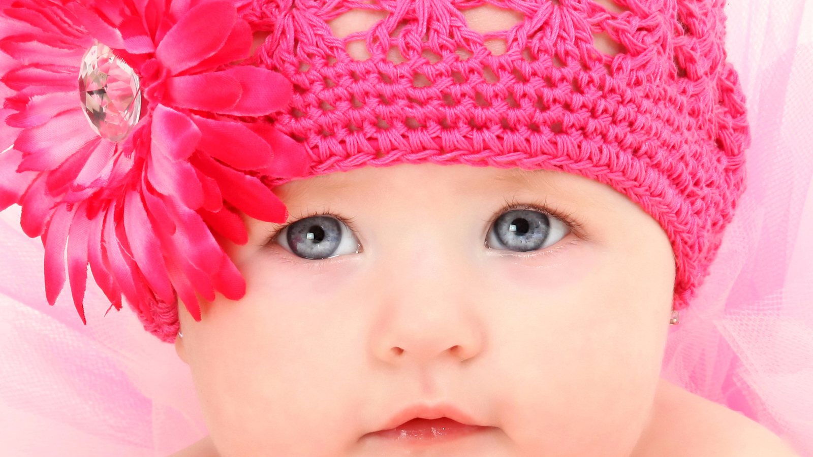 Милая голубоглазая малышка в розовой шапке с цветком герберы