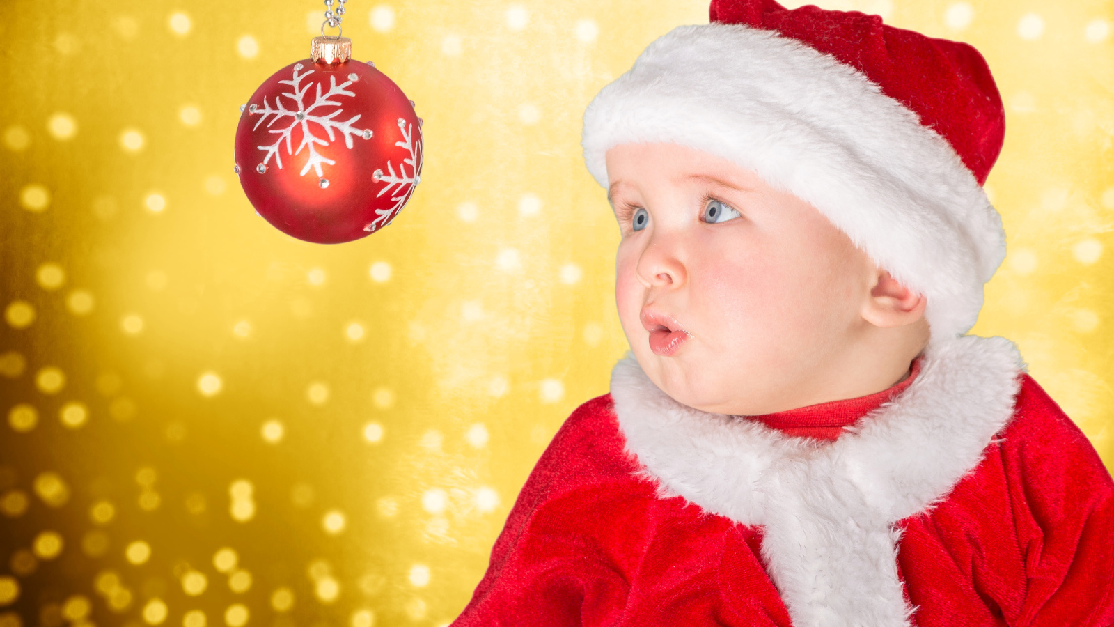Маленький грудной ребенок в костюме Санты смотрит на елочный шар