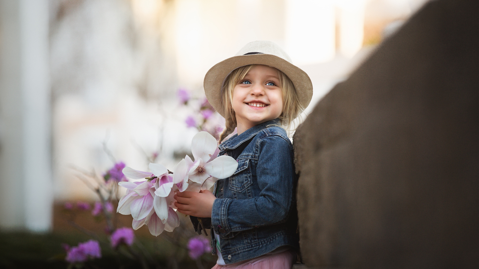 Маленькая голубоглазая улыбающаяся девочка в шляпе с букетом в руках