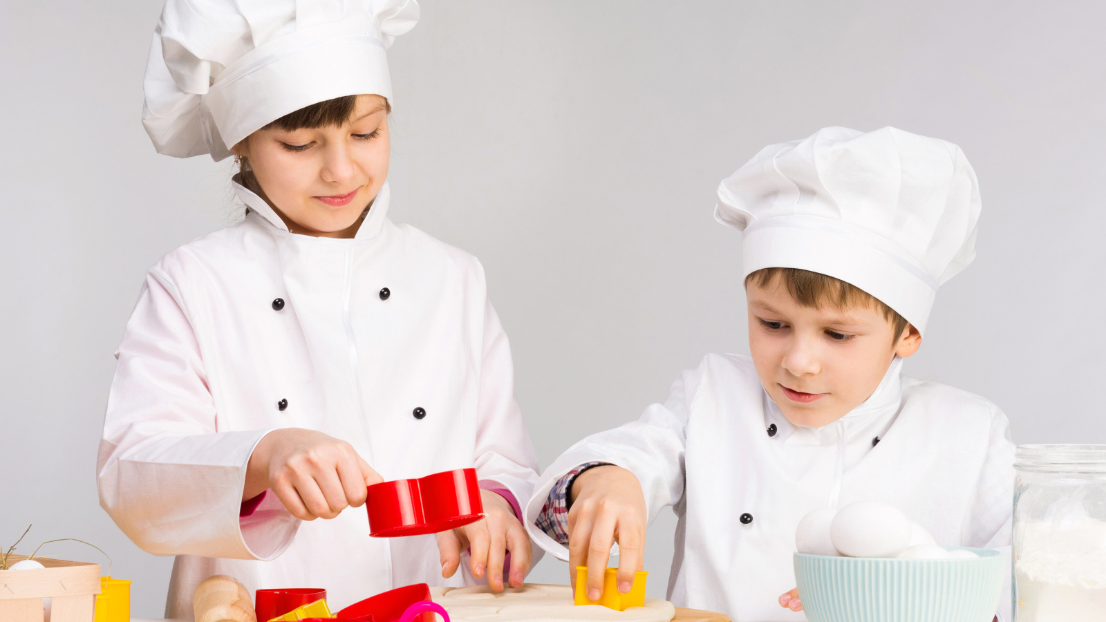 Маленькие мальчик и девочка готовят на кухне печенье