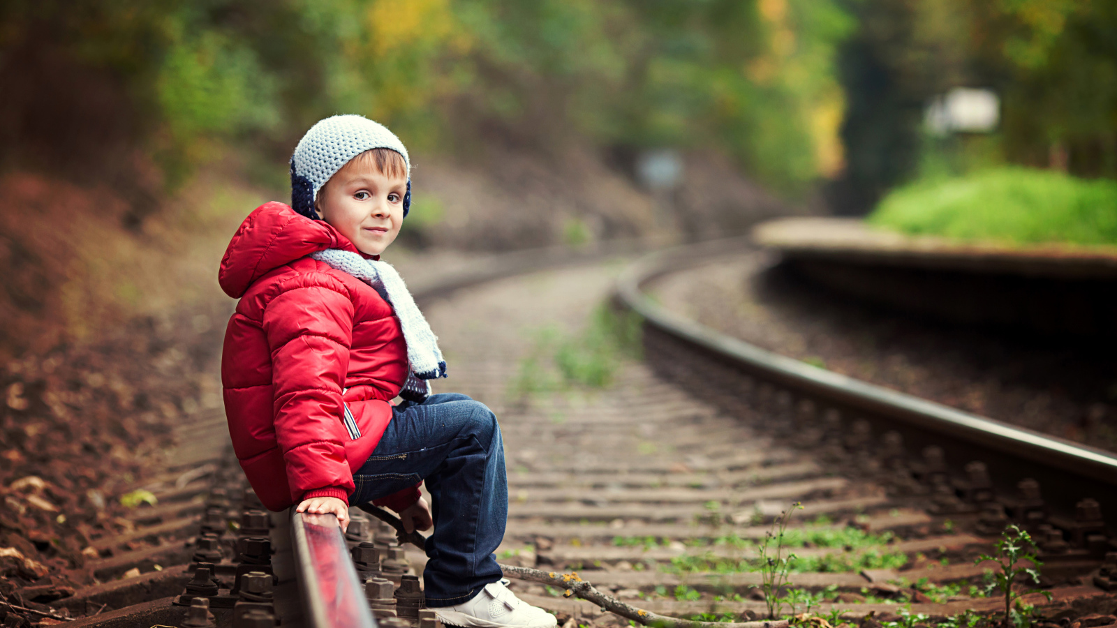 Маленький мальчик в красной куртке сидит на рельсах