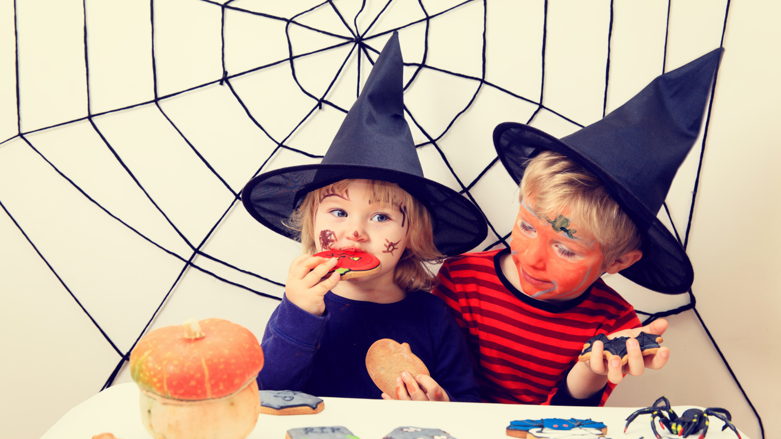 Маленькие дети в костюмах на Хэллоуин едят праздничные сладости