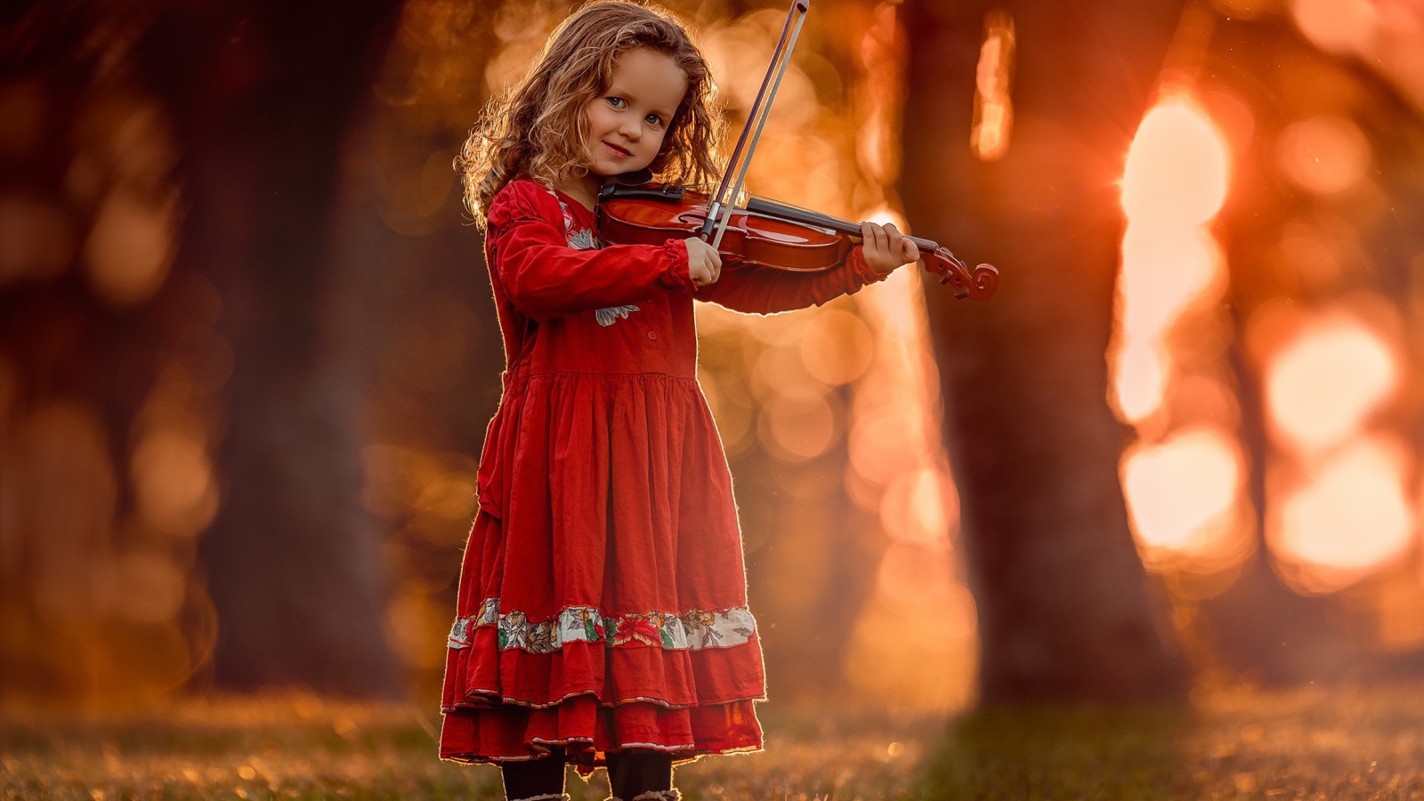 Маленькая девочка в красном платье со скрипкой в руках 