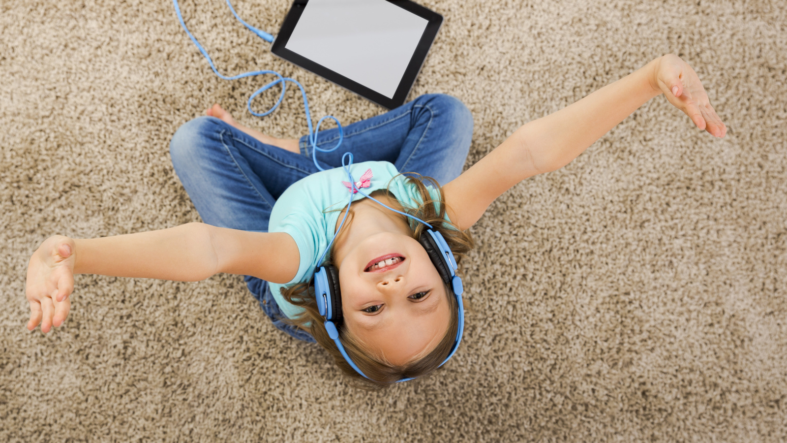 Маленькая девочка слушает музыку в наушниках сидя на ковре