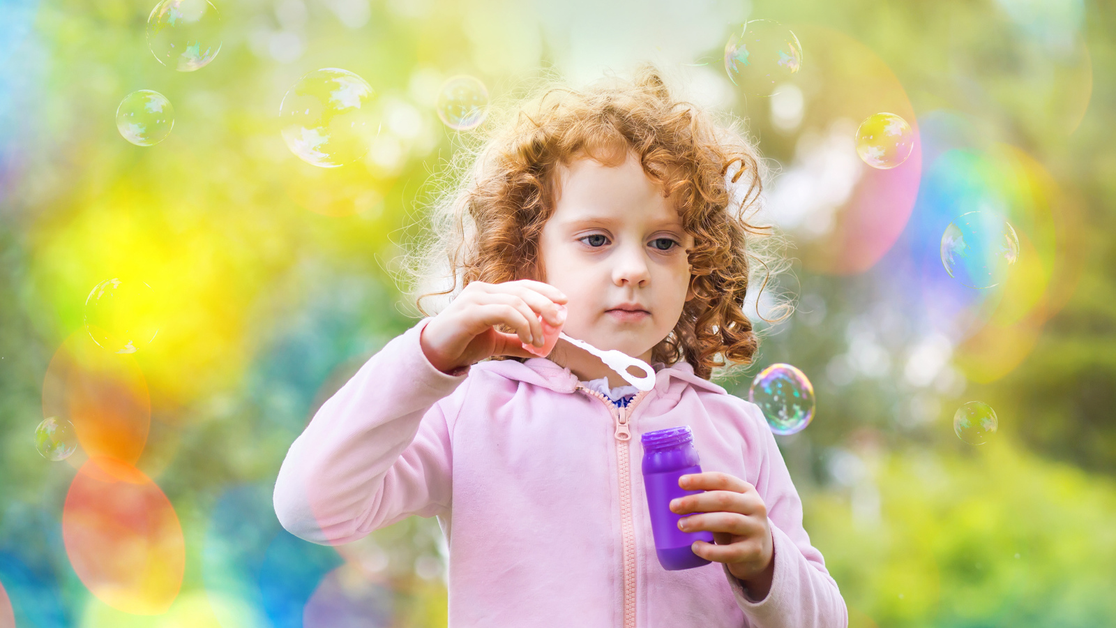 Маленькая рыжеволосая кудрявая девочка с мыльными пузырями