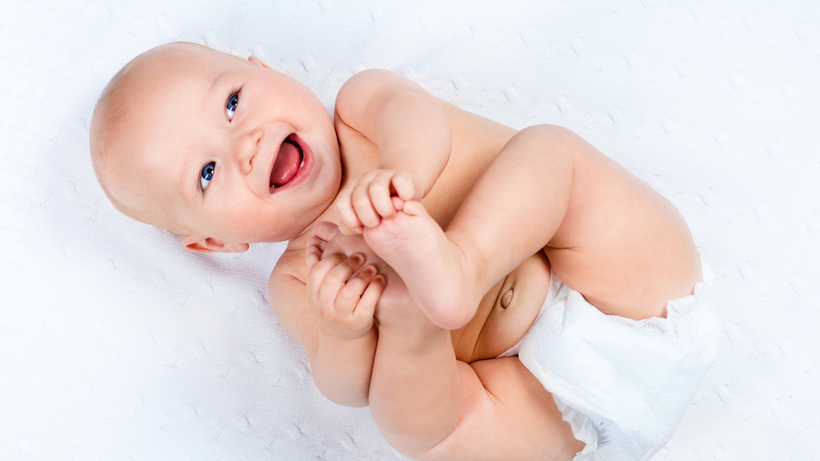 Маленький улыбающийся грудной ребенок держит руками ноги