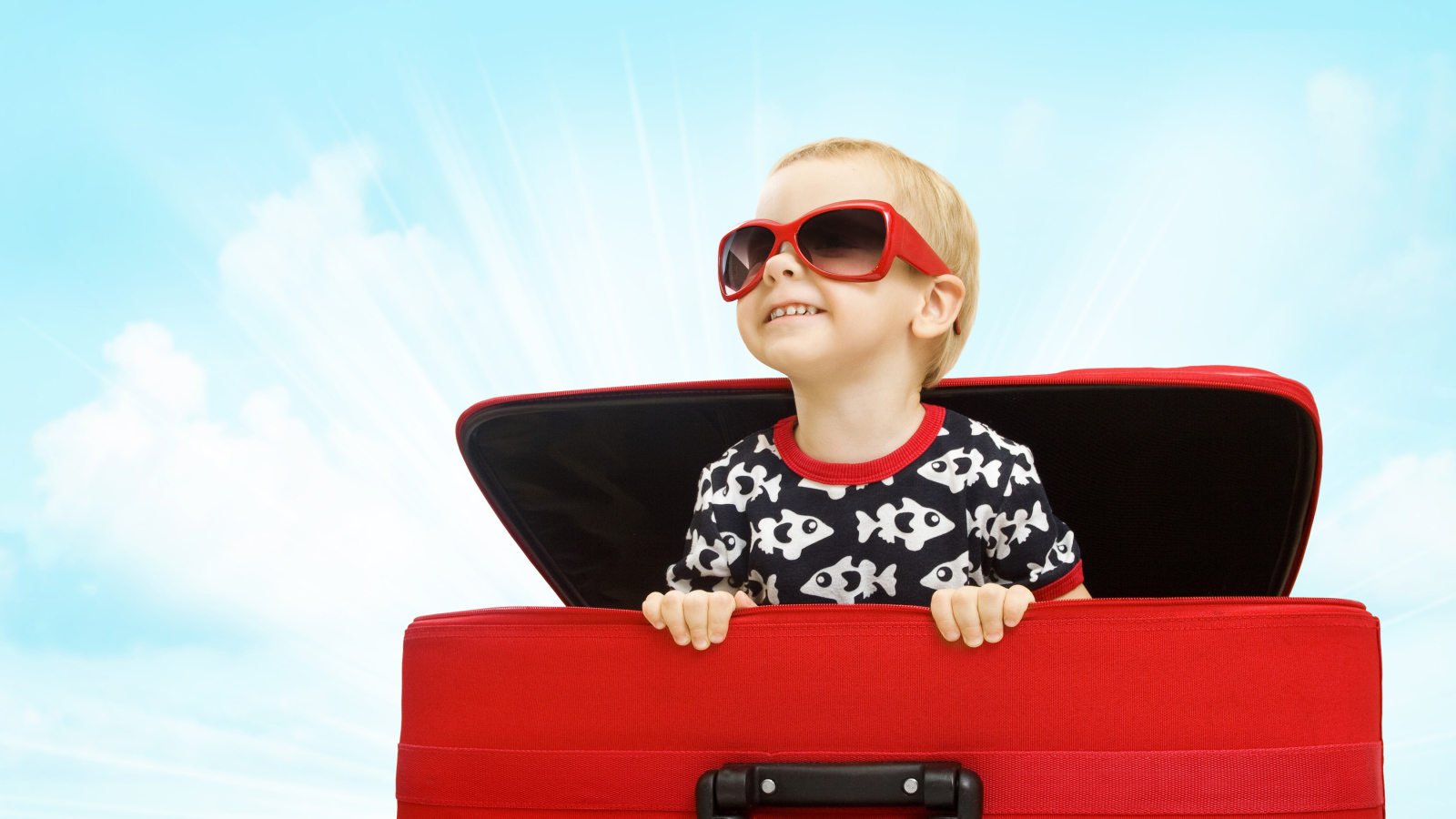Маленький улыбающийся мальчик в очках сидит в красном чемодане
