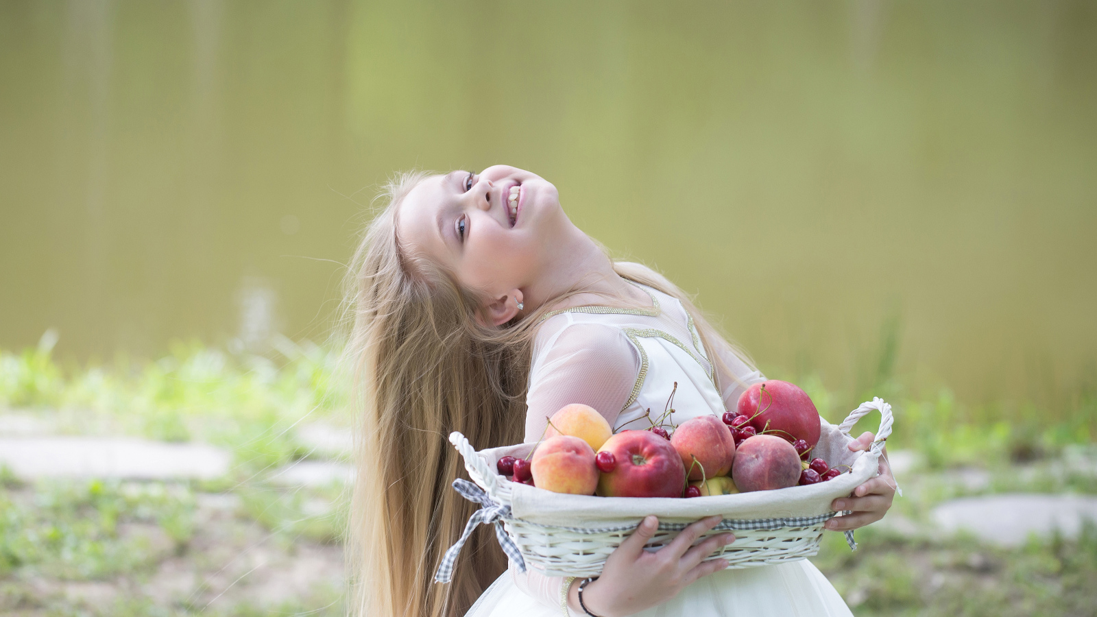 Маленькая улыбающаяся девочка в белом платье с корзиной фруктов