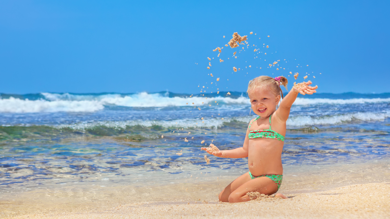 Маленькая улыбающаяся девочка играет на пляже с песком