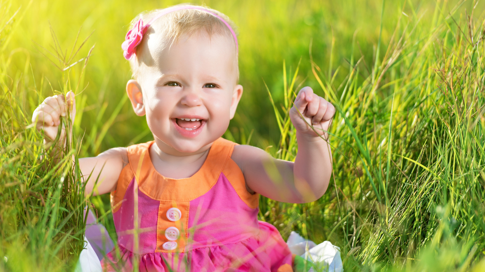 Маленькая улыбающаяся девочка сидит в зеленой траве