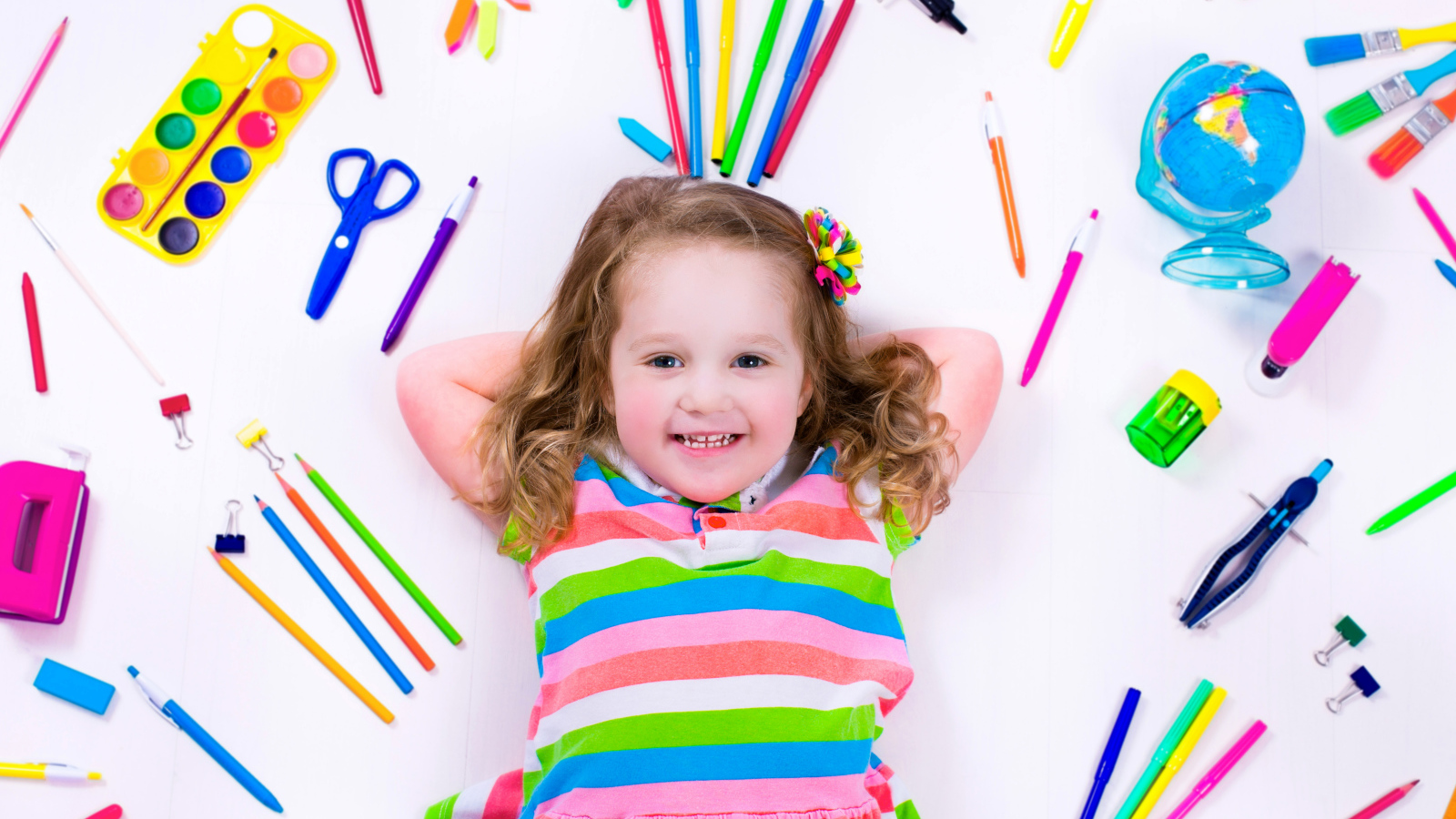 Маленькая улыбающаяся девочка со школьными принадлежностями