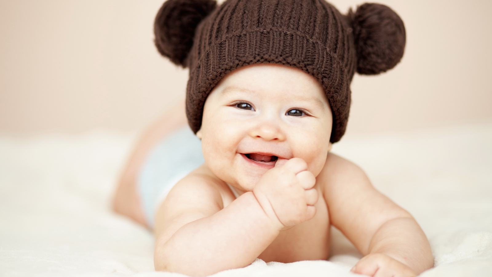 Улыбающийся грудной ребенок в коричневой вязаной шапке