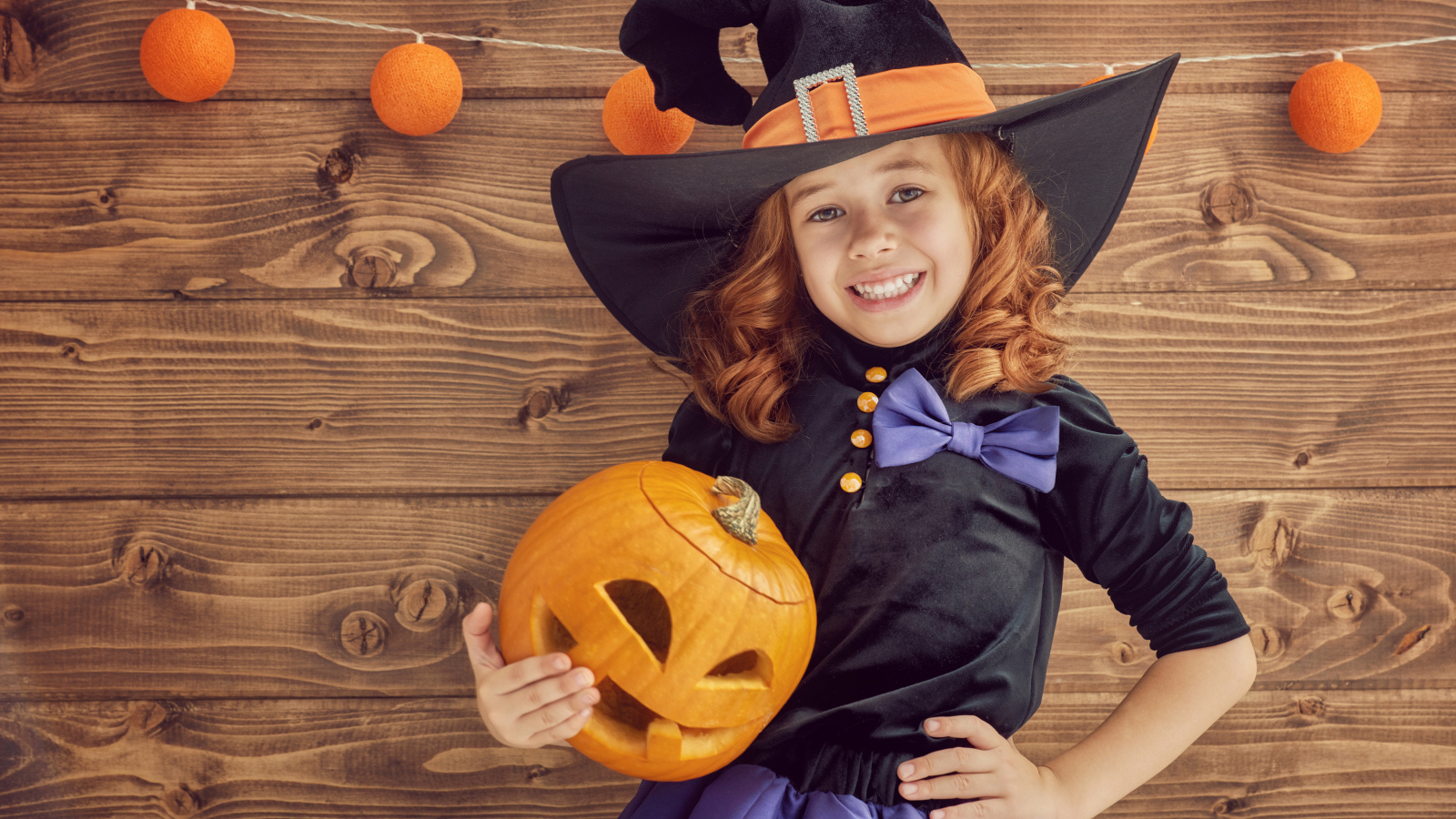 Улыбающаяся маленькая девочка в костюме ведьмы с тыквой на Хэллоуин