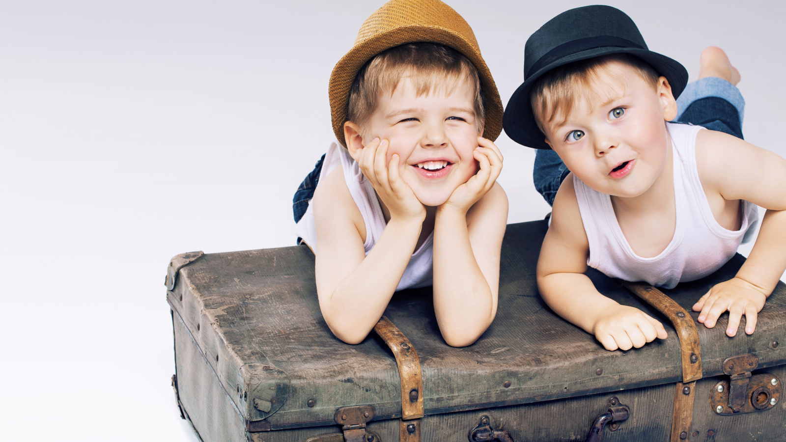 Два маленьких улыбающихся мальчика лежат на старом чемодане
