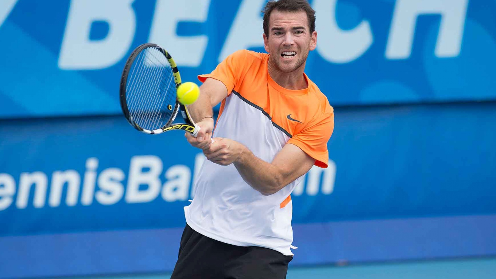 Теннисист Адриан Маннарино отбивает мяч ракеткой 