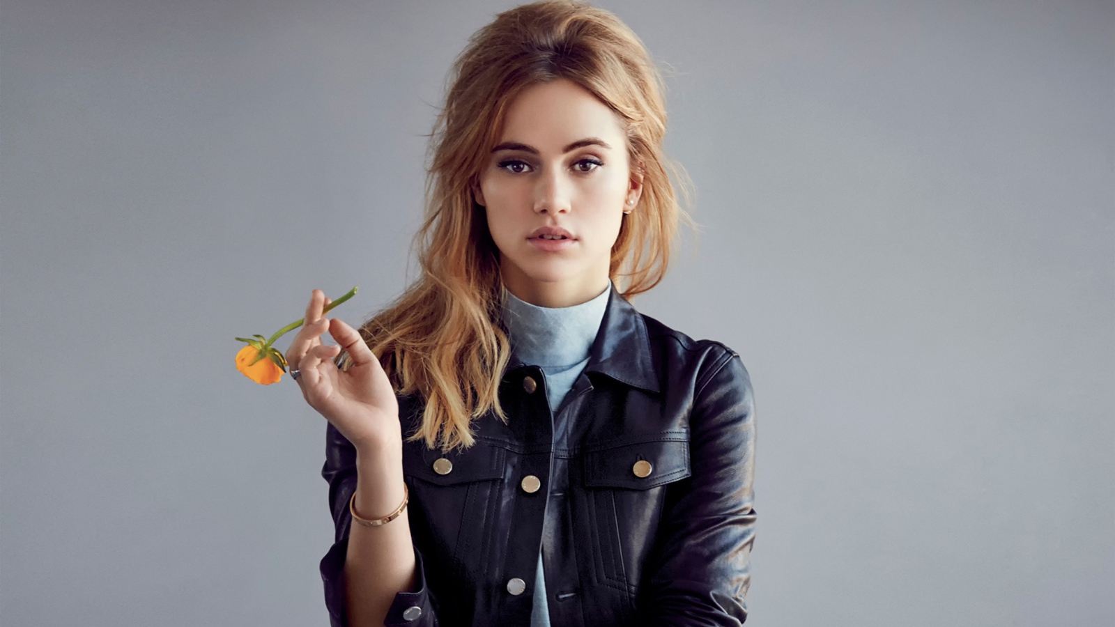 Актриса Сьюки Уотерхаус с цветком в руках на сером фоне