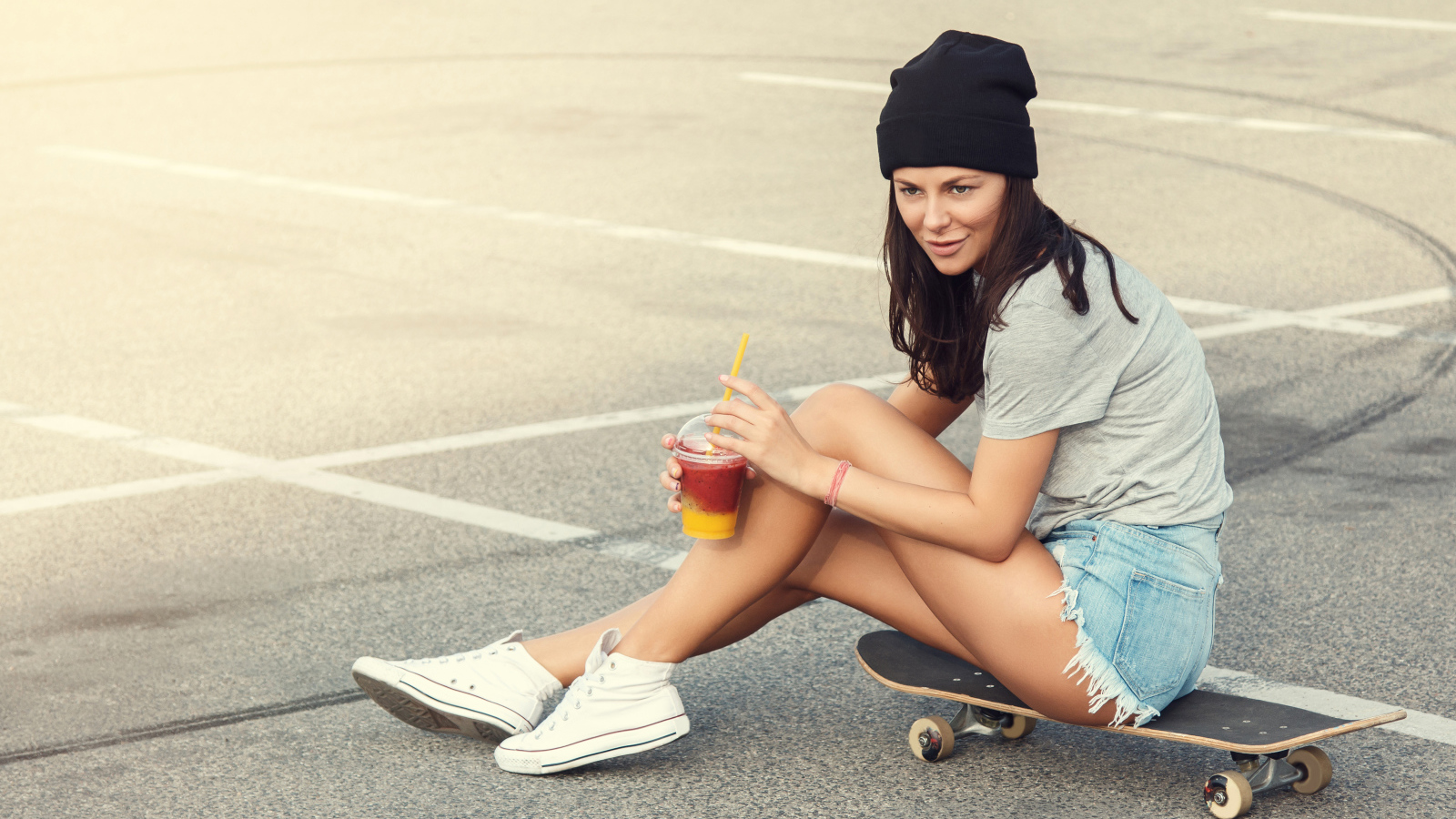 Спортивная девушка сидит на доске для скейтборда 