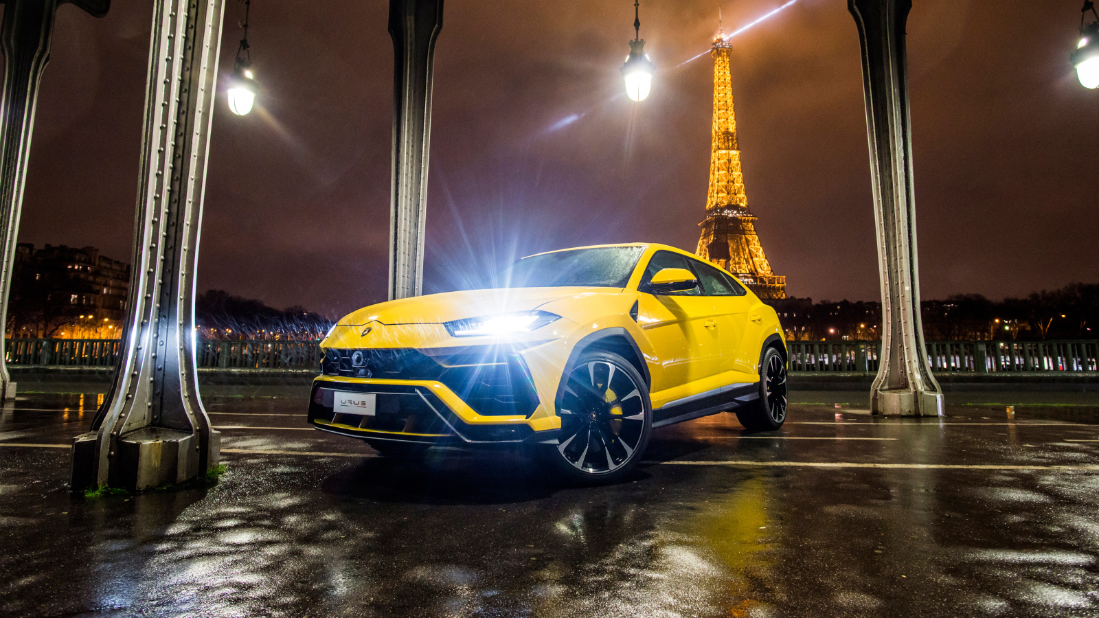 Желтый Lamborghini Urus, 2018 с включенными фарами на фоне Эйфелевой башни