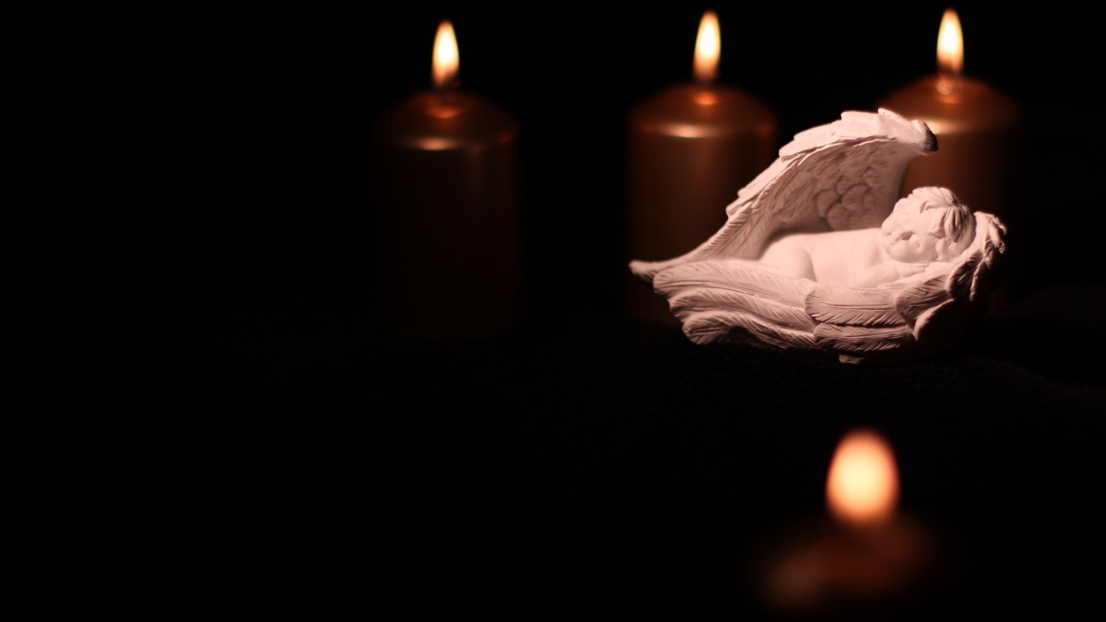 Фигурка ангела освещен горящими свечами на черном фоне