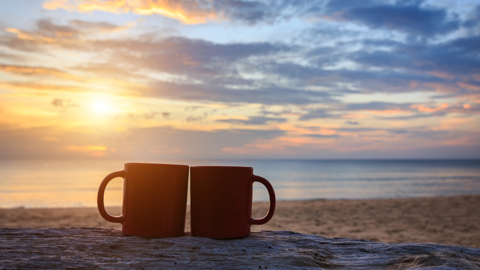 Две чашки стоят на песке на фоне рассвета 